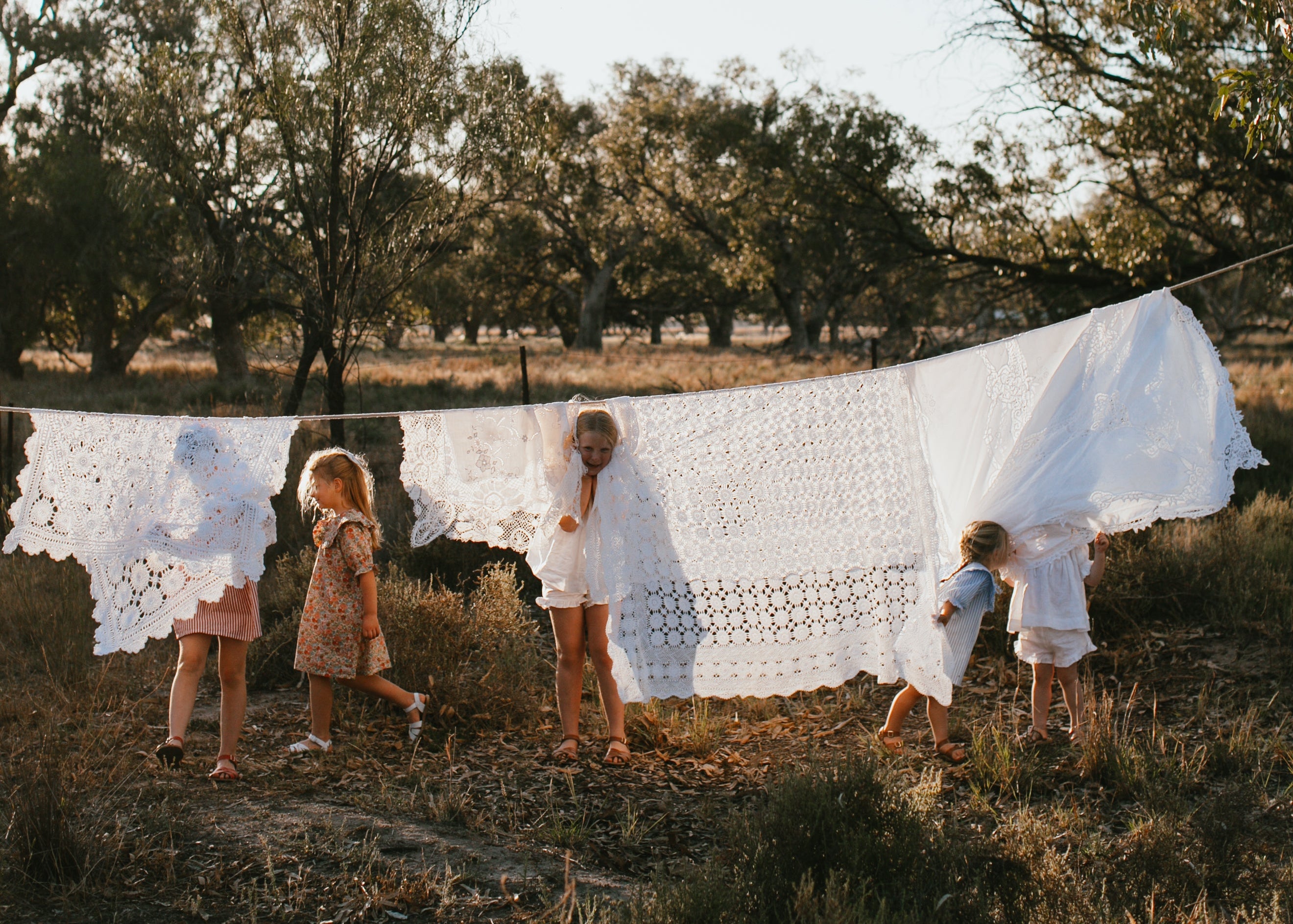 Children playing with white cloths on a line in a natural setting