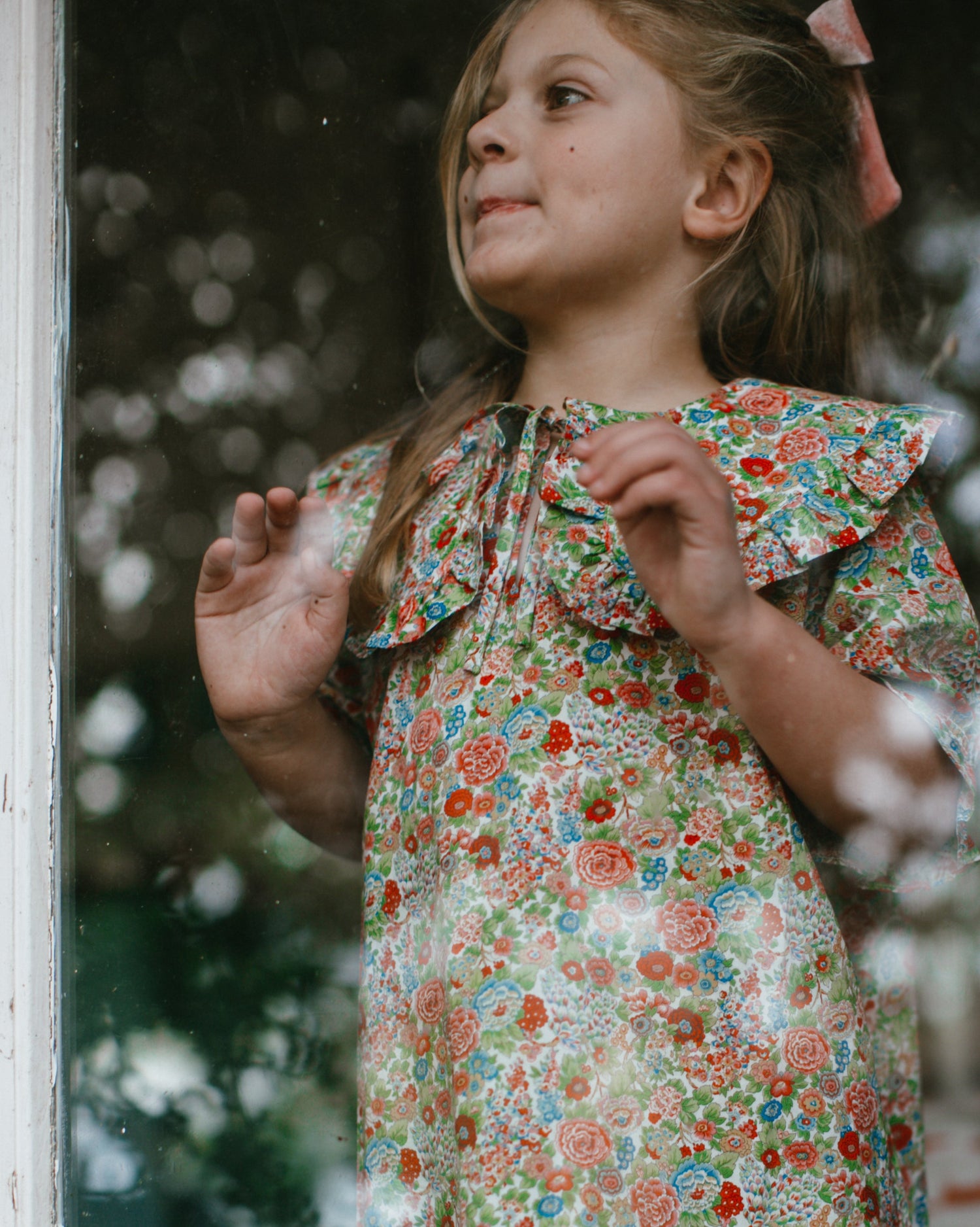 Young girl wearing a floral dress standing outdoors with blurred background